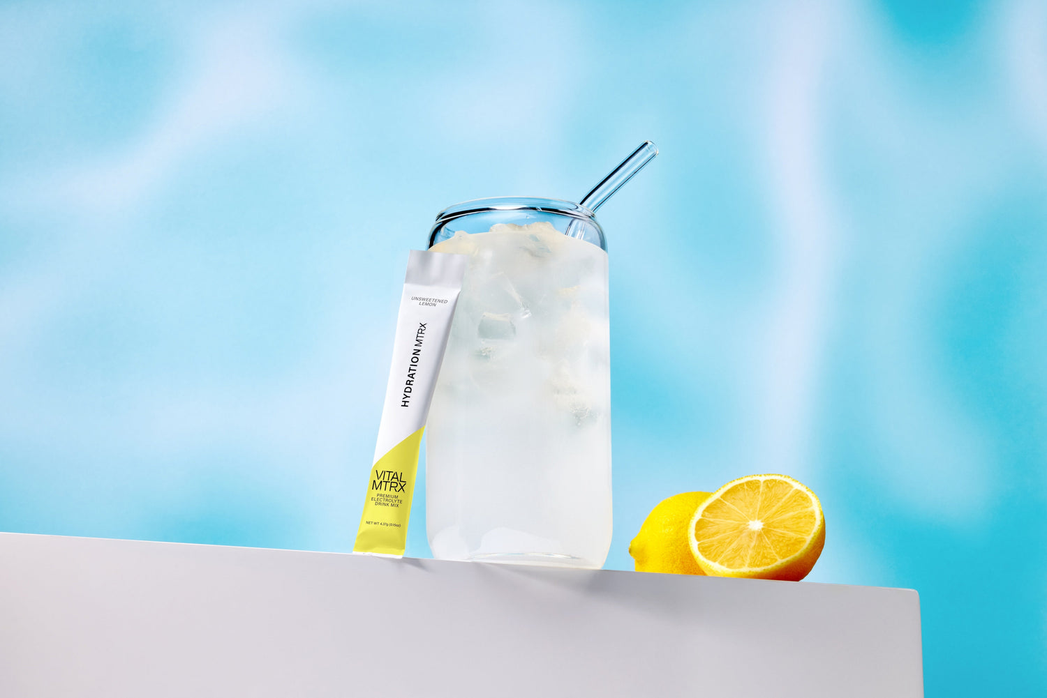 Glass of lemon electrolyte with a straw, lemon slices, and a Hydration Mix packet on a light blue background.

